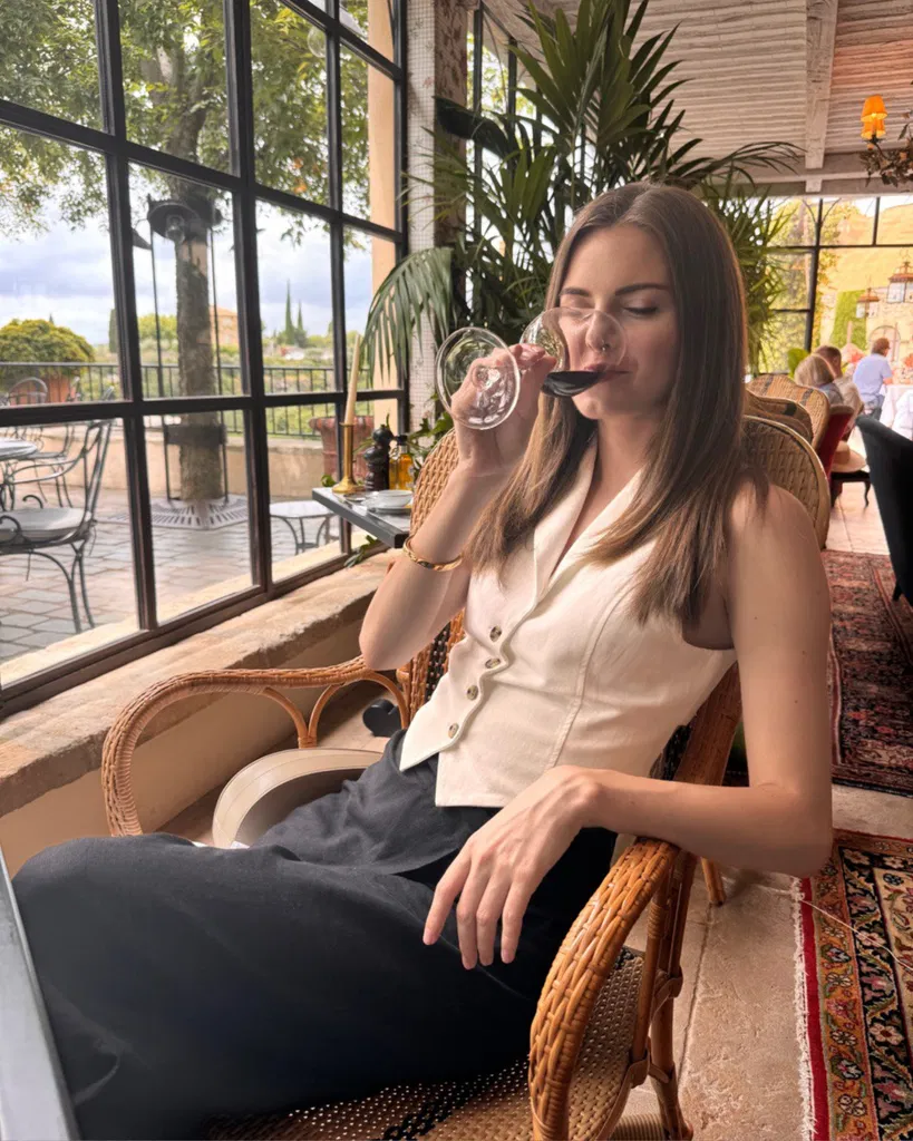 Anastasia assise dans un café en train de boire un verre de vin