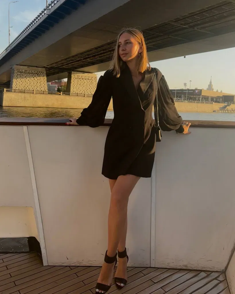 Maria en plein pied dans une robe noire courte à manches longues, avec un pont en arrière-plan