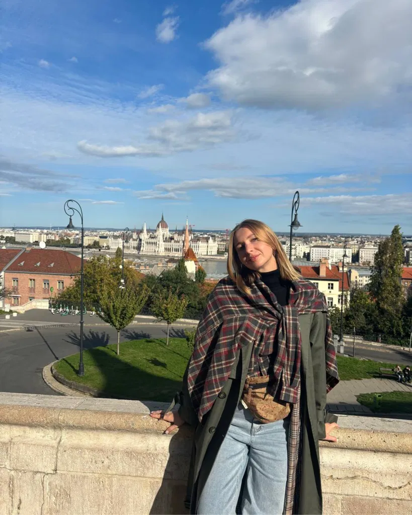 Maria devant un paysage urbain à Budapest, avec l’immeuble du Parlement au loin