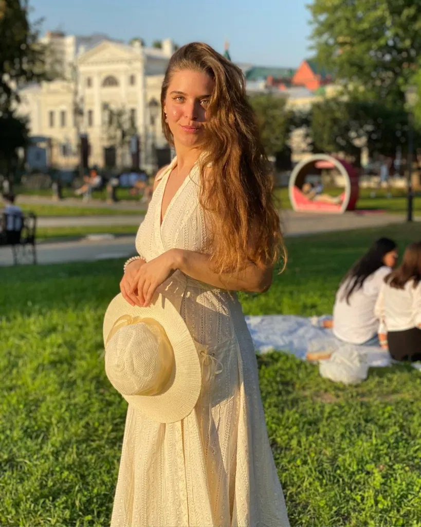 Olga avec de longs cheveux détachés dans une robe claire, sur fond de parc